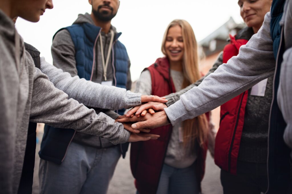 Close up of group of happy community service volunteers stacking hands together outdoors in street